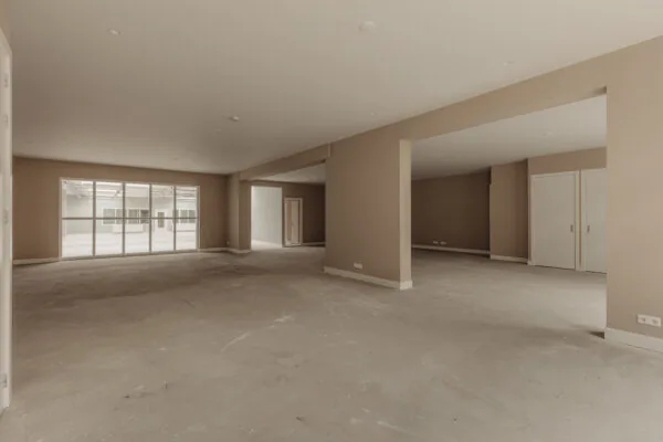 Ruime, lege binnenruimte aan de Henri Polaklaan met beige muren en grote ramen naar een atrium.